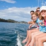 a family smiling and leaning over the railing of their boat at sea