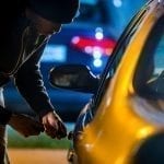 Thief breaking into car at night with a screwdriver