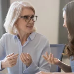 a younger woman and an older woman talk together in front of a computer
