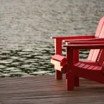 two red wooden reclining chairs on a boat dock next to a lake